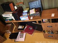 Overview of wooden desk with assorted books, binders, black and red folders, wooden desk holders, and small boxes of supplies on and under the desk.