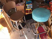 Photo showing two vintage stools and a black step stool among other household items and boxes.