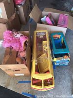 Overview of the lot showing yellow Barbie bus, Barbie dolls including one in a pink dress, boxes and case in the background