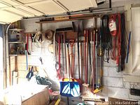 Full view showing various yard tools hung on a wall including snow shovels, rakes, shovels, broom, and cords hanging
