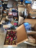 Wide view of boxes showing door decor, gift bags, string lights, bulbs and poinsettia packaging