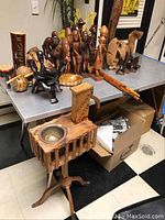 Overview of carved wooden figurines, carved coconuts, maracas, pipes, walking sticks, and planter stand.