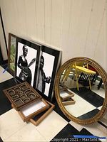 Group photo of oval mirror with gold floral frame, three framed black and white art prints, and wooden shadow boxes, all standing against a wall.