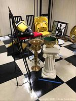 Photo showing black metal easel stand, brass champagne bucket, ceramic pedestal planter, glass vase, and framed photos.