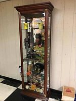 Full front view of the dark wood curio cabinet filled with various collectibles showing door, glass shelves, and lighted interior.