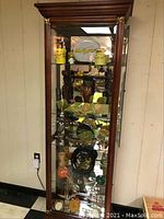 Full view of wooden and glass display cabinet with multiple shelves containing assorted travel souvenirs and memorabilia.