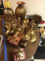 Overview of brass decorative items on a table including vessels, animal figurines, candle sticks, bell