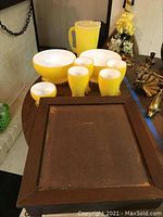 Full view of the yellow plastic cups, bowls, handled pitcher, and wooden tray on a table.