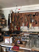 Wall pegboard with hanging hand tools including hammers, pliers, saws, clamps; shelves with boxes and power tools visible.