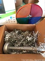 Box containing the color wheel showing four colored segments and part of the tree base with attached silver tinsel branches.