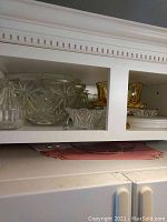 Wide view of cabinet shelf showing multiple glass punch bowls and smaller dessert bowls along with amber colored decorative items.