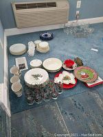 Overall view showing plates, teacups, glasses, and glass serving pieces arranged on carpet, featuring Christmas and gold-trimmed designs.