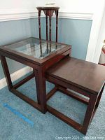 Three wooden furniture pieces including a glass top table and two wood tables/stand positioned in corner.