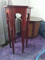 Tall wooden stand with four legs and cut-out design, reddish finish, showing wear.