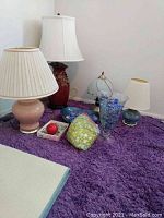 Four assorted lamps on a purple rug including glass and ceramic styles with shades and unshaded items.