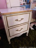 Front view of the nightstand showing two drawers with decorative gold handles and gold trim on the edges.