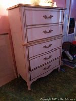 Front angle view of tall chest of drawers showing five drawers with ornate metal handles and wood trim detail.