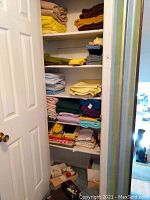 Closet with multiple shelves holding folded sheets, towels, blankets, tablecloths, and napkins in assorted colors and fabrics.