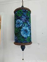 Full view of the hanging lamp with its cylindrical floral fabric shade and pull chain below.