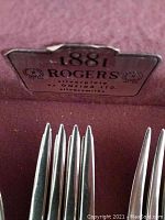 Close-up photo of 1881 Rogers silverplate flatware in maroon case, showing branding and arrangement of forks and spoons.
