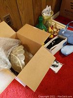 Overview of items including shell lamp packed in a cardboard box, various decorative items arranged nearby on red carpet.
