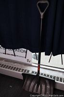 Full view of the snow shovel showing the metal shaft, wide black plastic blade, and D-handle.