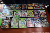Lot of PC games featuring several Sims titles including base games and expansions, Grand Theft Auto IV and Call of Duty Black Ops II, all cases shown on a table.