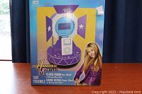 Box front showing the Hannah Montana clock radio with digital display and image of Miley Cyrus.