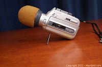 Side view of Sony micro-cassette recorder showing microphone with orange foam windscreen and device branding on wooden surface.