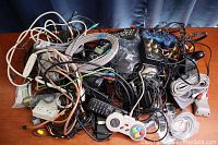 Overview of the tangled collection of wires, controllers, remotes, and adapters laid on a wooden surface.