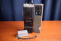 Two vintage Realistic handheld radios on a wooden surface with a blue background, showing the front and side of each radio and their antennas.