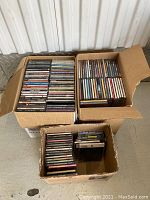 Three cardboard boxes filled with over 200 CDs in jewel cases, showing a variety of album spines and artists.