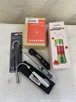 Photo showing boxed Inkbird Smart Wireless BBQ Thermometer, boxed Supkitdin Portable Blender, and two black digital BBQ thermometers with probes outside box.