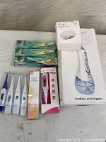 Lot contents laid out on a white cloth surface showing oral irrigator in box, 9 thermometers (some boxed, some loose) and toothbrush covers.