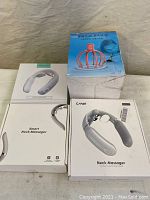 Photo showing 4 boxed massagers including 3 neck massagers (ANLAN and CAHOT brands) and 1 pink octopus-shaped head massager. Boxes mostly white with product images.