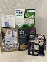 Boxed baby bottle sterilizer, Philips Avent bottle set, Tommee Tippee Closer to Nature gift set, Braun breast pump, and other baby bottles shown in original packaging and boxed condition.
