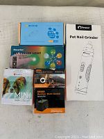 Boxed dog collars, trays of bark control devices, and pet nail grinder in original packaging placed on a beige surface.