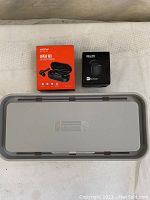 Top view of two wireless earbuds boxes and a gray cable management box lid.