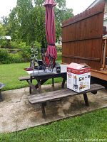 View of wooden picnic table from one side showing attached benches and closed burgundy umbrella in the center.