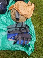 Two adult medium life vests and a rolled-up green tent bag laid out on a green tarp on grass.