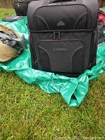 Front view of black Tourmaster motorcycle bag with large zippered compartments on a green tarp outdoors.