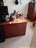Photo showing one side of the wooden L-shaped office desk with a smooth reddish-brown finish in an office setting, accompanied by some office accessories on top.