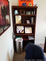 Front view of the wooden bookcase showing five shelves with various items and decorative crown molding on top.