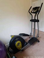 Side view of ProForm elliptical showing flywheel and pedals, placed against a wall on carpet.