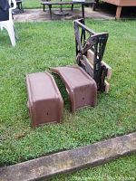 Two brown metal fender covers and metal jack stands lying on grass