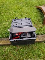 Black Craftsman plastic carrying case partially open on grass containing the red and black chainsaw and accessories inside.