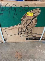 Photo showing front of the box with Hitachi brand, saw illustration, and handwritten price $99.00