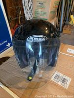 Black Gmax motorcycle helmet with clear platinum tint shield, placed on cardboard box.