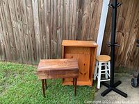 Full view of all four furniture items: wooden bookcase, drop leaf table, stool, and hat stand on grass outside a wooden fence