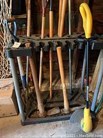 Photo of multiple yard tools with wooden handles on a black metal and plastic tool rack